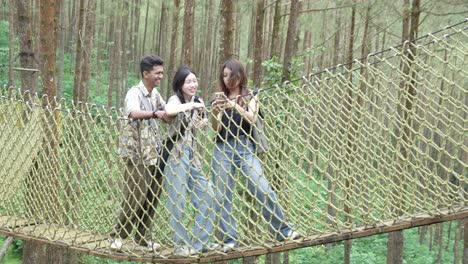 asian friends taking selfie on forest rope bridge in indonesia