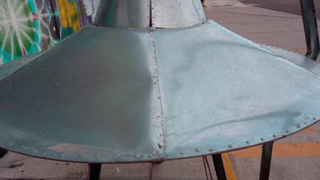 zoom in on a silver ufo model outside a store with alien-themed graffiti art and props, under daylight