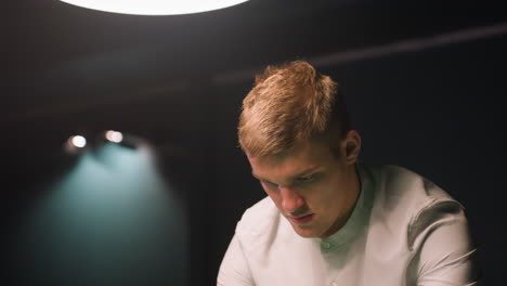 close-up of young man in off-white shirt, deeply focused with calm concentration against dark background. soft overhead lighting casts subtle glow on his face