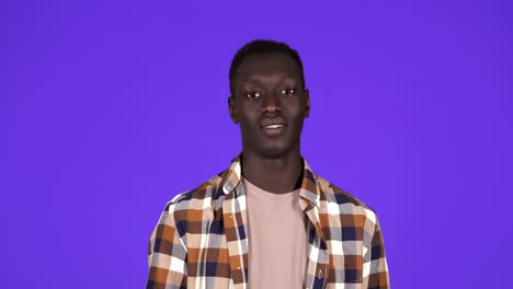 Strong-afro-american-young-man-wearing-plain-shirt-isolated-on-blue-background-in-studio-showing-muscules-at-camera,-sportsman.-People-sincere-emotions,-lifestyle-concept