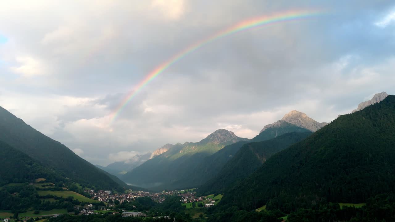 Aerial drone view of Val di Scalve in the Italian Dolomites and Alpi Orobie, featuring a dramatic and vivid rainbow over the rugged alpine landscape