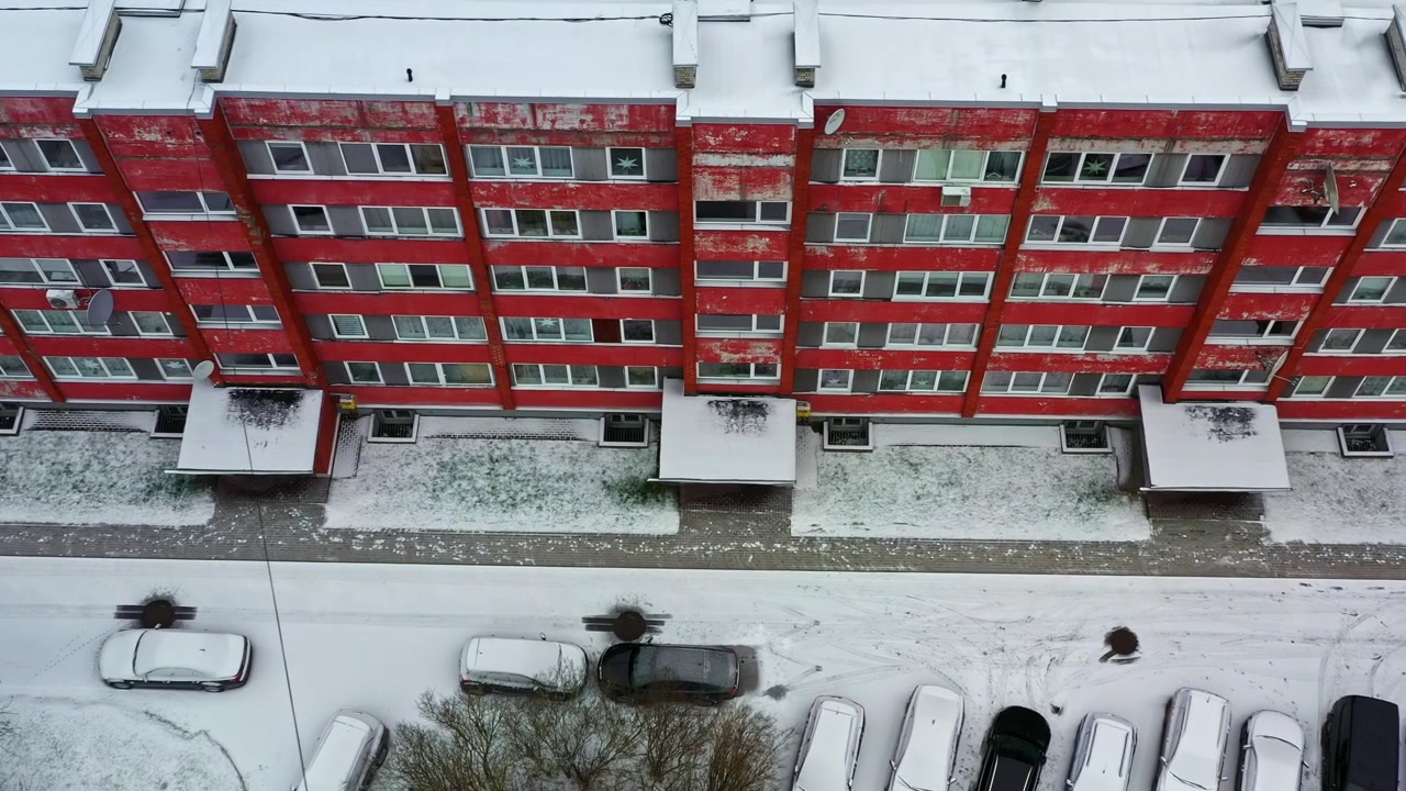 Lejlighedsbygning fra sovjettiden og snedækkede biler på en parkeringsplads, luftfoto ovenfra