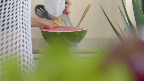 a woman cuts a watermelon with a large knife in the kitchen