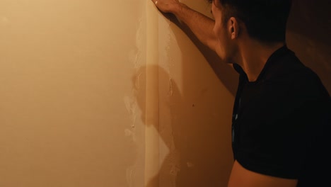 un joven mide las tiras protectoras en la pared antes de empapelar