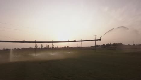 Advancing-aerial-of-irrigation-pivot-near-highway,-backlit-by-sunset