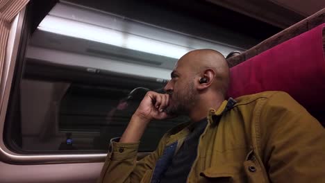 pensive south asian man with wireless earphones looking out the window while traveling by train passing through a dark tunnel