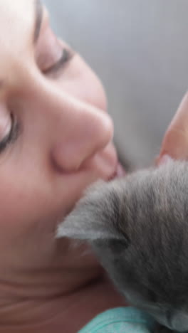 smiling woman lying on couch cuddling tiny kitten