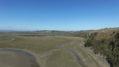 Aerial-view-along-the-side-of-cliff-on-the-coast-of-north-west-England-at-low-tide,-on-a-bright-sunny-day