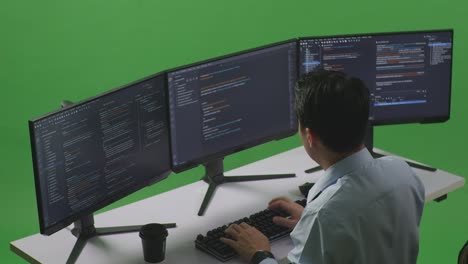 vista lateral de un desarrollador asiático que tiene dolor de cabeza mientras escribe código con múltiples pantallas de computadora en el estudio de pantalla verde