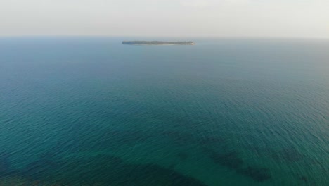 Drone-shot-gentle-descent-looking-out-into-the-distance-on-a-remote-island-with-reefs-and-turquoise-seas-in-the-foreground