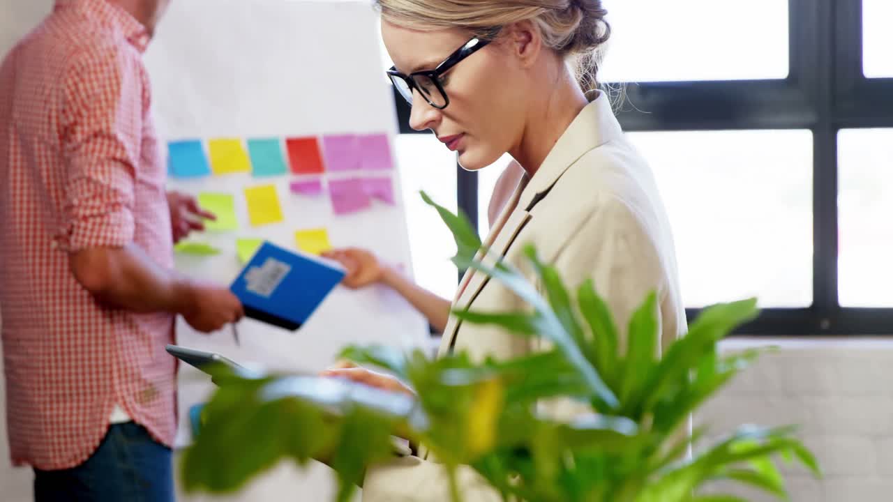 ejecutiva usando una tableta digital mientras sus colegas discuten en la pizarra blanca