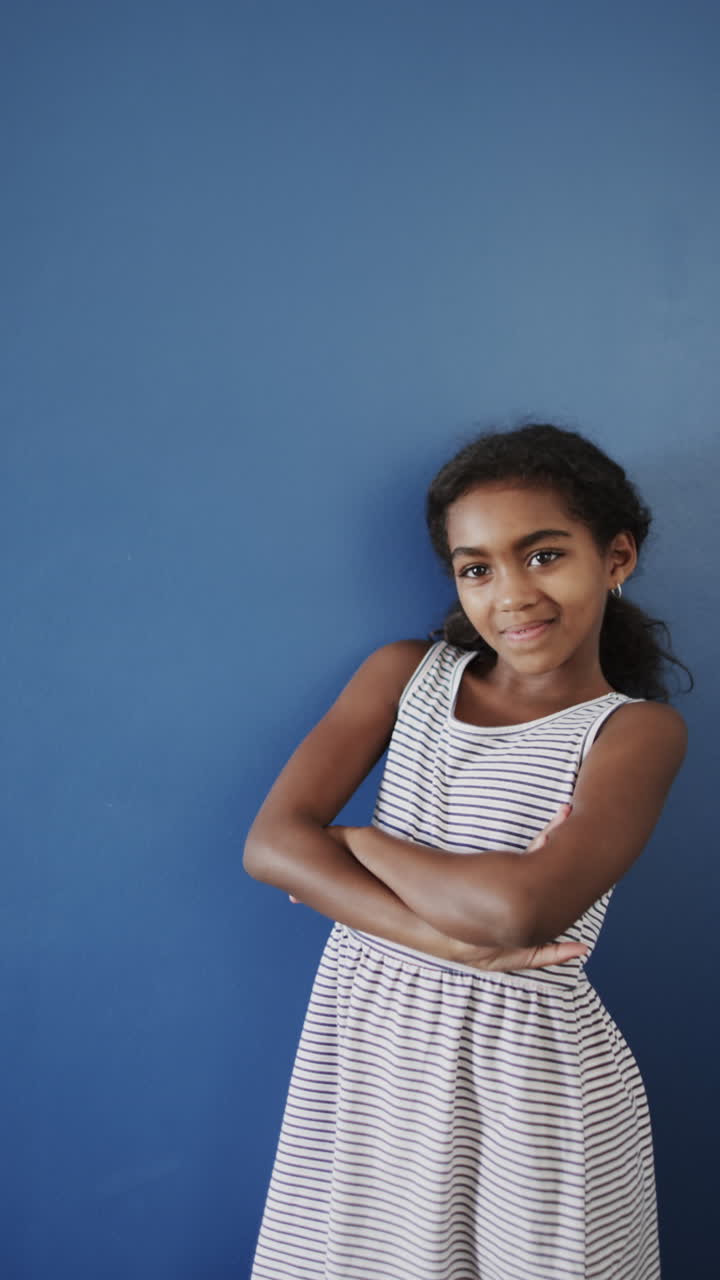 Vertical video of happy biracial girl smiling on blue background, slow motion