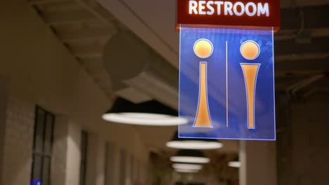 Stock clip of fancy upscale modern design restroom sign lit up led lights up tall on ceiling in industrial studio building with huge lamps in background
