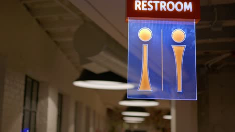 stock clip of fancy upscale modern design restroom sign lit up led lights up tall on ceiling in industrial studio building with huge lamps in background