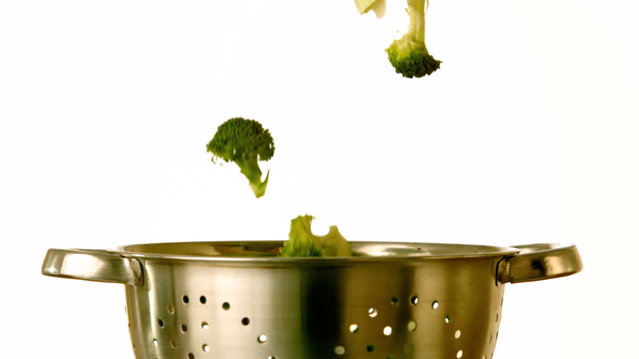 Broccoli falling into colander on white background