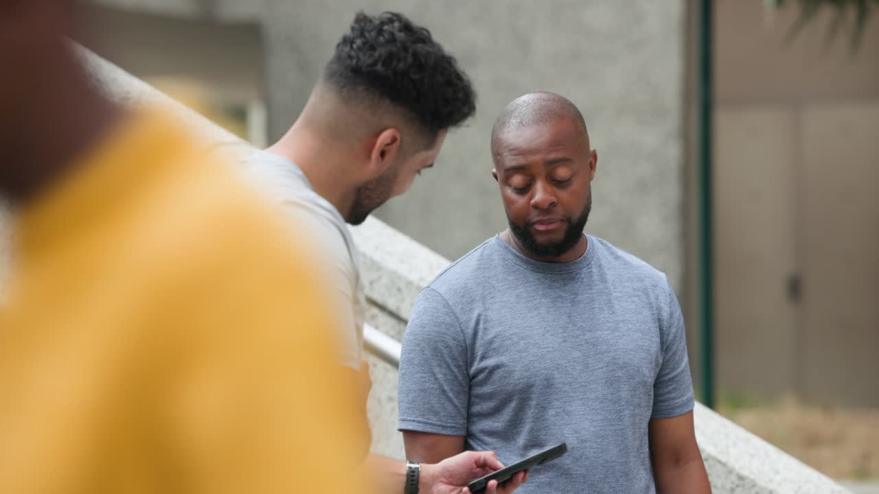 Diverse male friends chatting at plaza stair railing, unlocking smartphone showing pic and laughing
