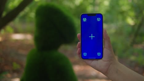 young woman holding phone chroma key screen in the green park close-up. girl with green screen on smart phone. nature