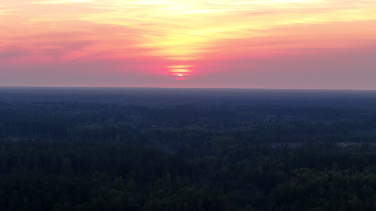 A tranquil sunset with fading yellow light behind orange pink diffused clouds, warm hues and scenic forest rural surroundings in Latvia