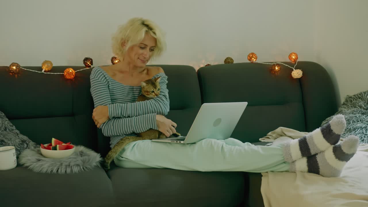 Woman relaxing on a couch with her cat and a laptop