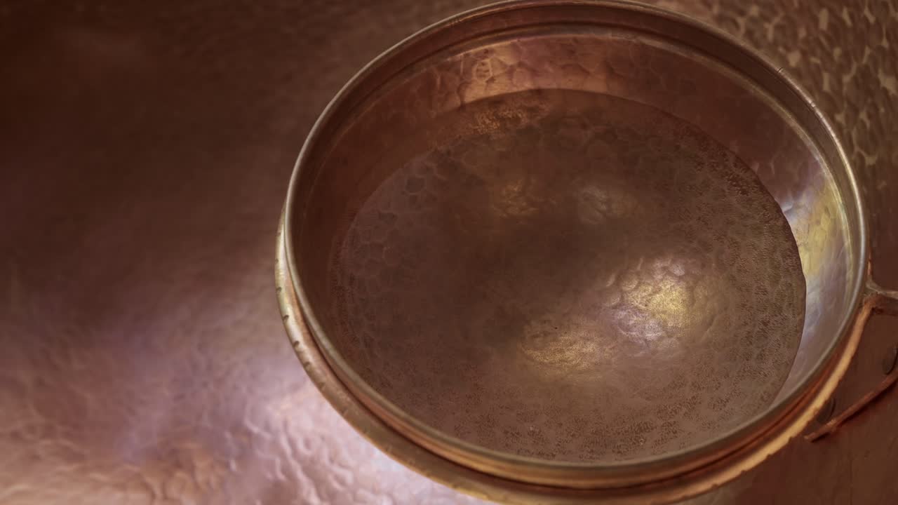 Cuenco de cobre martillado con agua reflejando la luz sobre superficie metálica