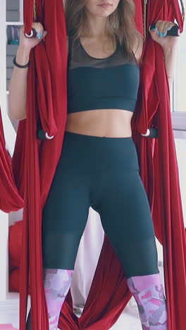 pretty ladies group sits in anti-gravity yoga warrior asana stands up holding long red hammocks close view slow motion