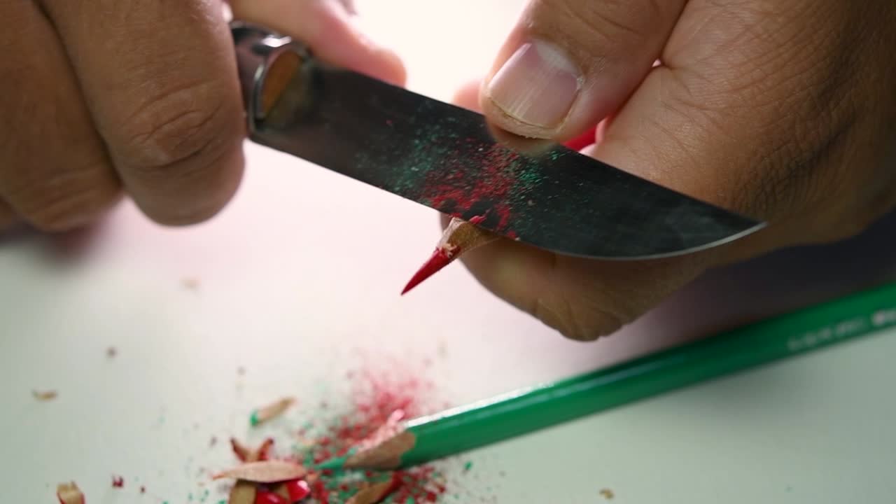 Opptak av hender som sakte spisser en blyant og noen fargeblyanter med en skarp kniv