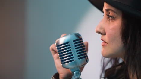 close side view of a singer wearing a black hat and holding a vintage microphone.,singer's facial profile and expression are highlighted against a white background as the camera zooms out