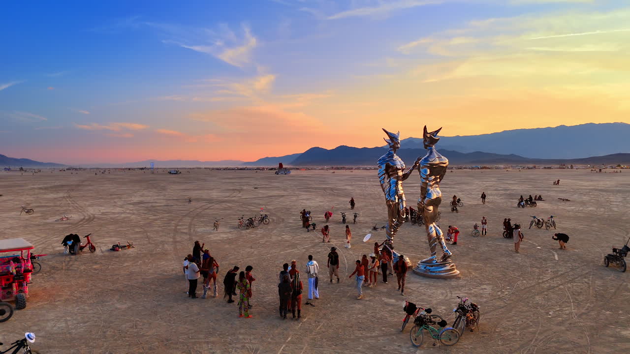 Nevada, USA, 14 August 2025: Festival crowd around metallic sculptures at Burning Man in Nevada desert.. Participants gather around silver sculptures on the playa at sunset