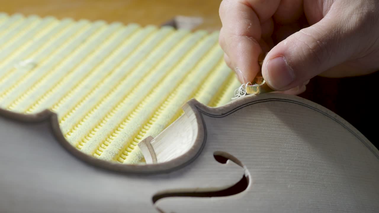 macro primer plano de artesano luthier fabricante de trabajo en nuevo clásico hecho a mano violín crudo borde liso en la cintura y raspado púrpura en el banco de trabajo del taller en cremona italia video 4k