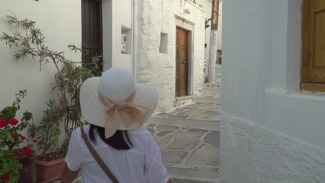 siguiente foto de una chica con traje de senderismo veraniego y sombrero caminando por el típico callejón griego estrecho