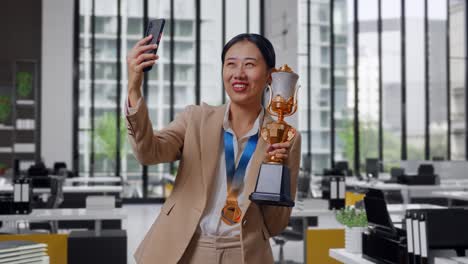 Asian Business Woman In A Suit With A Gold Medal Showing A Gold Trophy To The Video Call On Smartphone In The Office