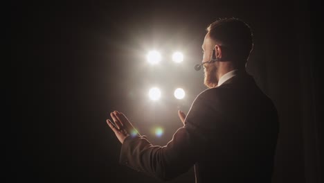 the speaker is conducting the conference. he is standing on the stage and talking into the microphone. he is waving his hands. the spotlight is shining on him. the camera is rotating around him. 4k.