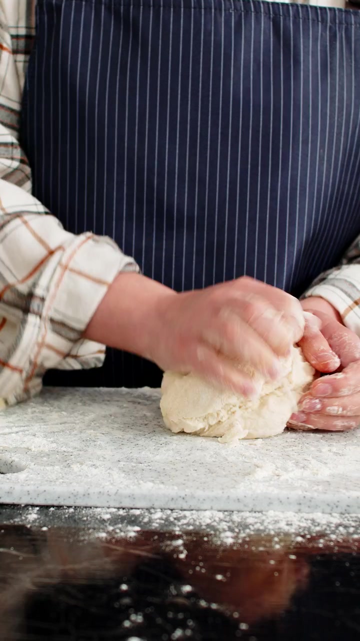 Young woman kneads dough on kitchen board with flour eggs milk and oil for baking bread rolls family