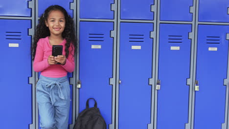 in a school hallway, a young biracial girl leans against blue lockers with copy space