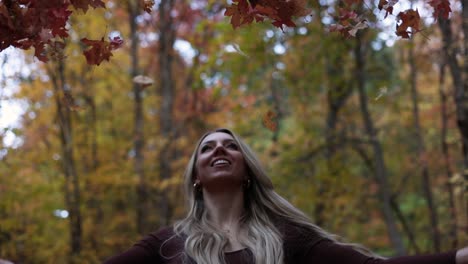 una mujer alegre arroja una hoja de arce al aire durante la temporada de otoño en el parque