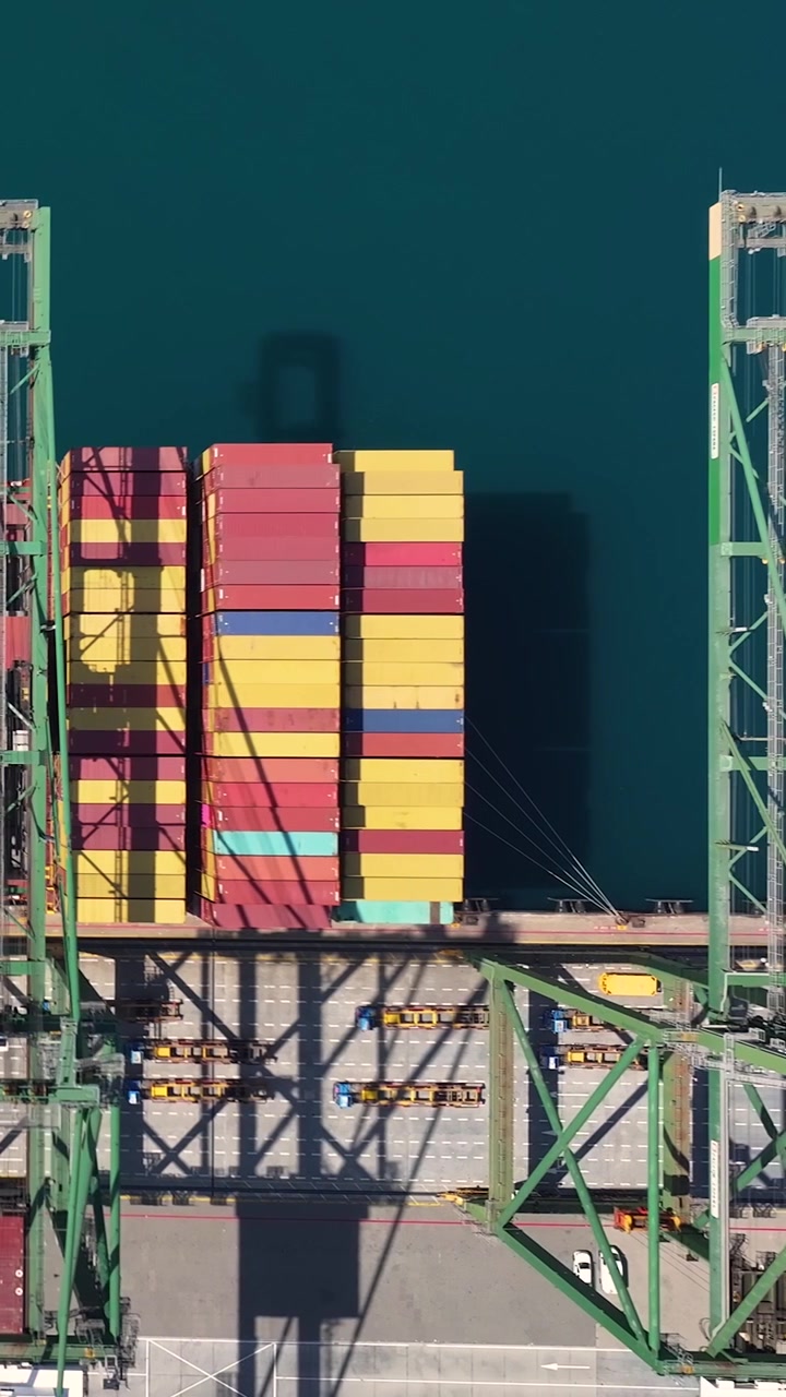 Container terminal shows shipping containers being loaded and unloaded. Cranes move freight at an international port during daylight. Activity highlights global trade efforts.