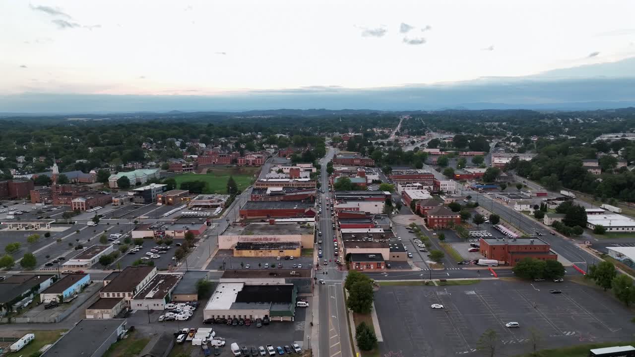 Red historic buildings in center downtown of waynesboro, Virginia. Aerial backwards shot. Parked cars on road at cloudy evening in summer. Rooftops of houses and homes. Wide shot