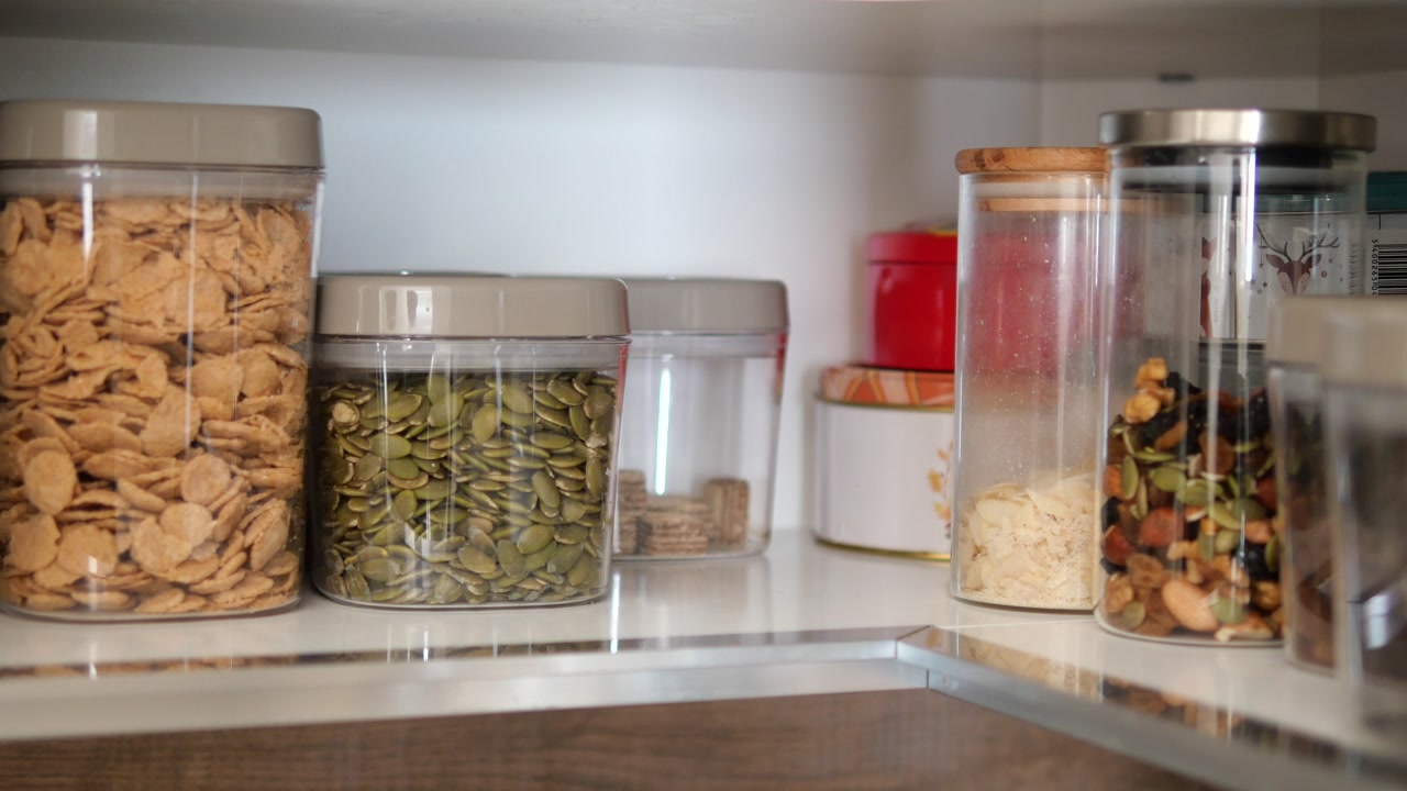 Hand Taking Cashews from Organized Food Storage Containers on Shelf