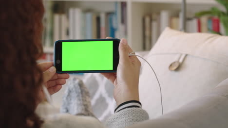 mujer en primer plano usando un teléfono inteligente viendo video de pantalla verde relajándose en casa en el sofá