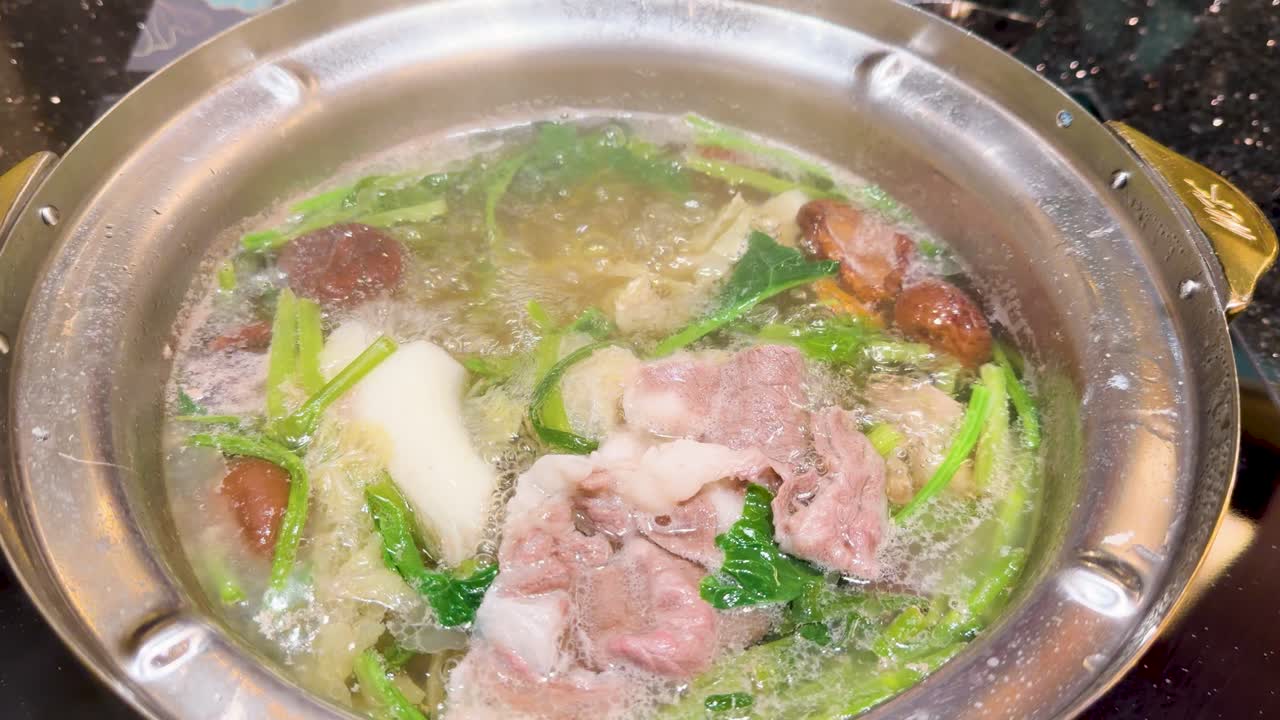 Sliced beef cooked with vegetables in bubbling hotpot broth, overhead view, bright lighting, minimal movement
