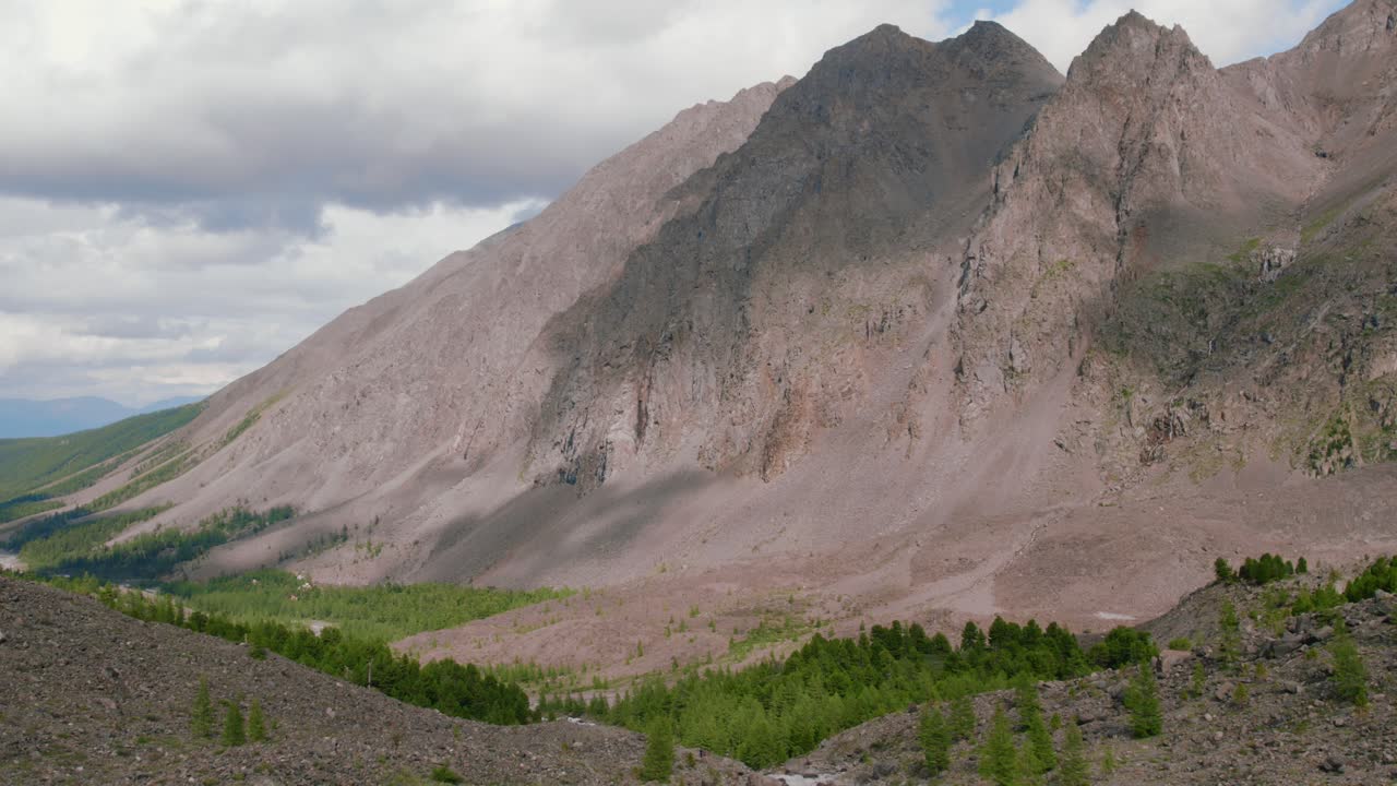 Ampia veduta di aspre montagne rocciose e una verde valle fluviale sotto un cielo nuvoloso nella Valle di Akturu, Repubblica dell'Altai, Russia, sfondo di viaggio suggestivo nella natura selvaggia.