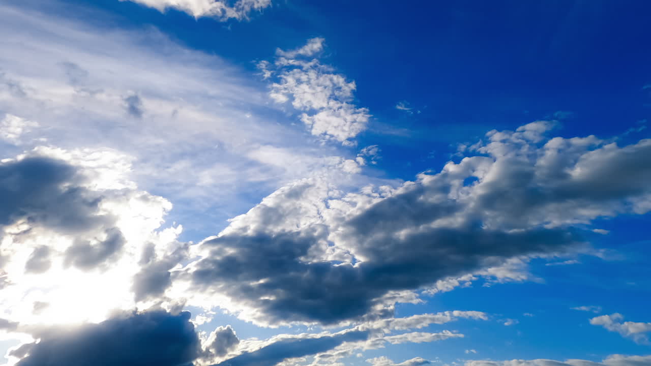 Grey fluffy cloudscape fly fast in the sky. Sun lighting the edges of soft clouds. Low angle view. Timelapse.