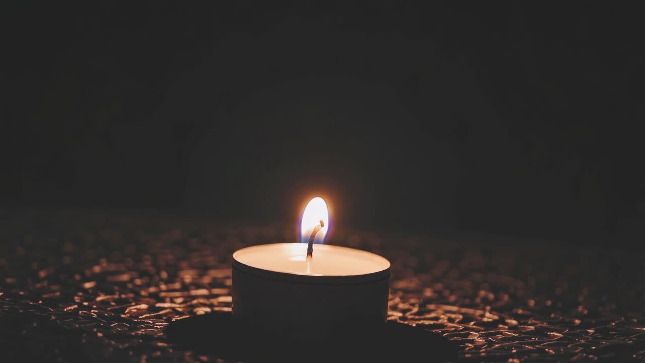 A close-up, low-angle video shot of a single lit candle on a textured surface, creating a serene