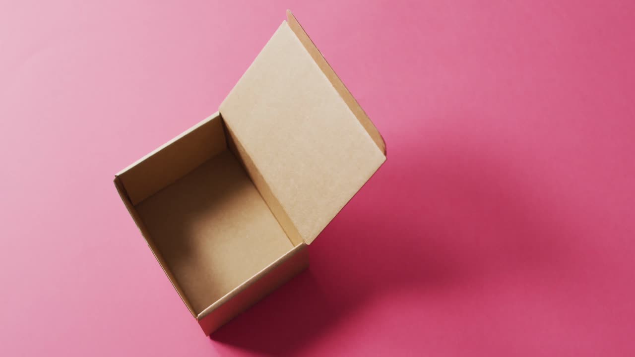 video de una caja de cartón abierta y vacía y espacio de copia sobre un fondo rosa