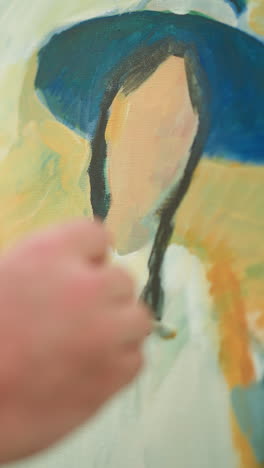 se ve la mano de un artesano, vestido con una camisa a cuadros, sosteniendo un pincel mientras pinta hábilmente y suavemente un retrato vibrante en un lienzo