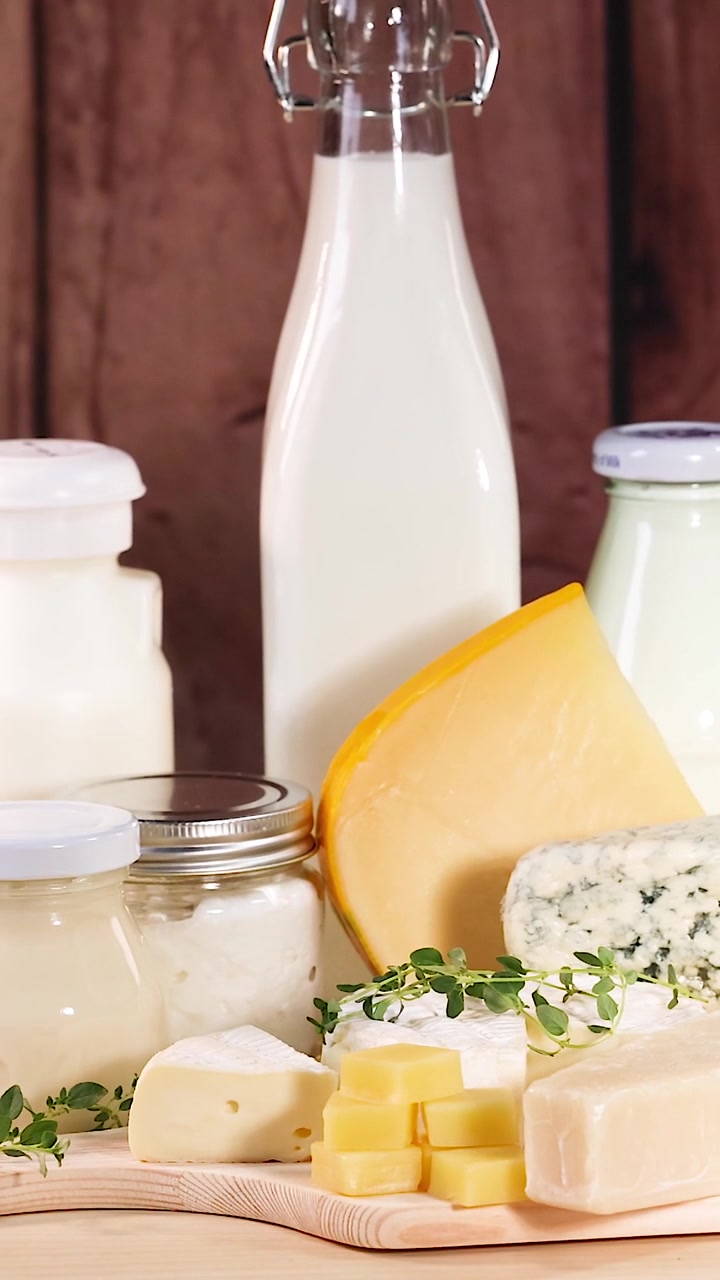 Una disposizione verticale di vari formaggi, bottiglie di latte e vasetti di yogurt su un tavolo di legno.