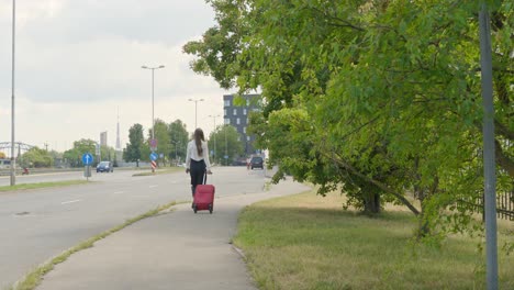 classy female tourist walking with red trolley on sidewalk