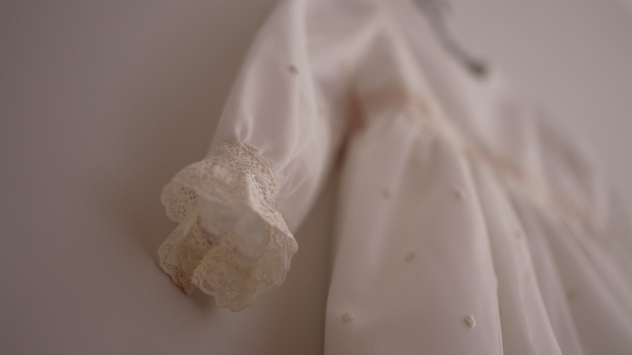 close up of lace sleeve detail on baby white dress hanging gently against soft light