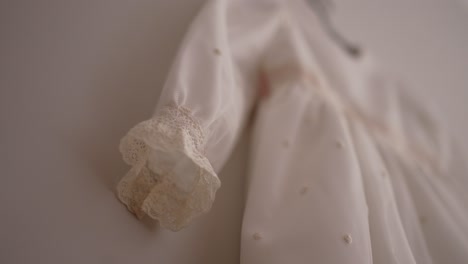close up of lace sleeve detail on baby white dress hanging gently against soft light