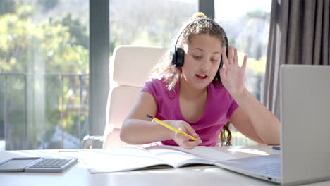 chica biracial feliz usando auriculares y portátil para la lección escolar en línea en casa